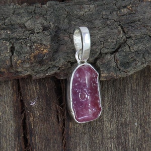 Peut inclure: Un pendentif en argent avec une pierre précieuse de rubis rose brut. Le rubis est serti dans une bélière en argent et a une forme naturelle irrégulière.