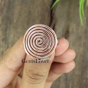 May include: A rose gold ring with a spiral design. The ring is made of metal and has a smooth finish.
