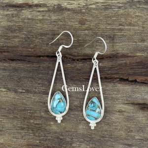 May include: A pair of silver dangle earrings with turquoise stones set in a teardrop shape. The earrings have a simple, elegant design and are perfect for everyday wear.
