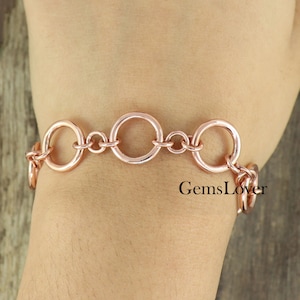 May include: A rose gold bracelet with a chain made of large, interlocking circles.