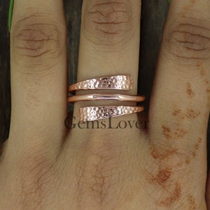 Pode incluir: Um anel de cobre martelado de ouro rosa com um design torcido. O anel &eacute; usado em um dedo.