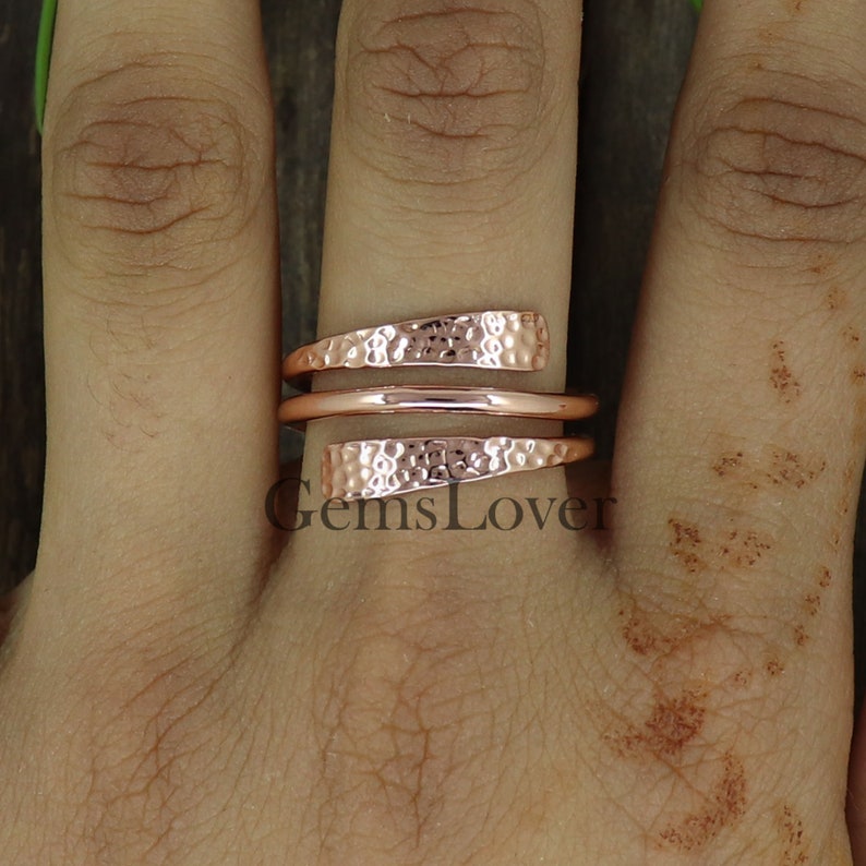 Pode incluir: Um anel de cobre martelado de ouro rosa com um design torcido. O anel &eacute; usado em um dedo.