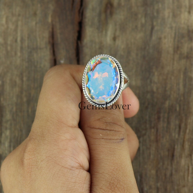 Peut inclure: Une bague en argent avec une grande pierre pr&eacute;cieuse ovale iris&eacute;e. La bague est sertie dans une bande d'argent avec un motif en forme de corde.