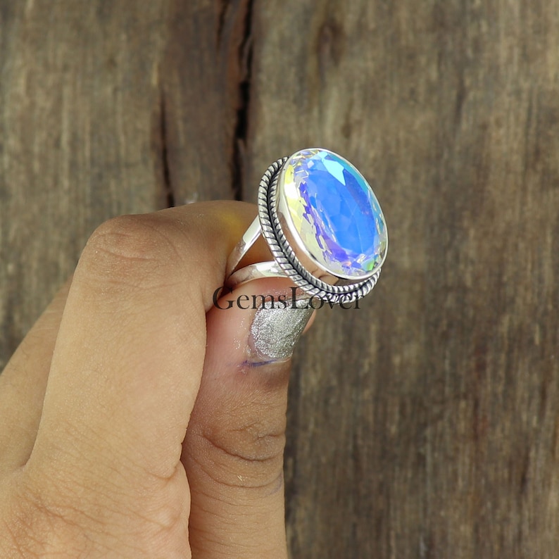 Peut inclure: Une bague en argent avec une grande pierre pr&eacute;cieuse ovale iris&eacute;e. La bague a une bande tress&eacute;e.