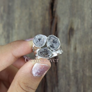 May include: A silver ring featuring three clear quartz stones set into the band. The stones have a rough, natural appearance. This ring is a unique and stylish piece of jewellery.