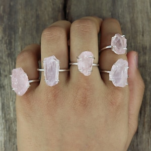 May include: Five silver rings with pink rose quartz stones. The rings are worn on a person's hand.