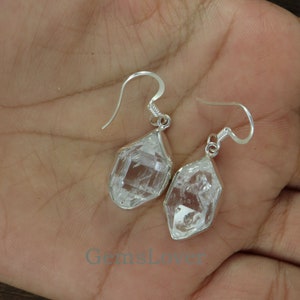 May include: A pair of silver earrings featuring clear quartz crystals. The crystals are faceted and have a geometric shape. The earrings are dangle style and have a hook fastening.