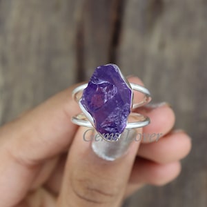 May include: A silver ring with a large, raw amethyst gemstone. The amethyst is a deep purple color and has a natural, irregular shape.