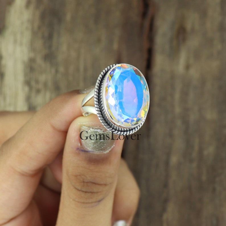 Peut inclure: Une bague en argent avec une grande pierre pr&eacute;cieuse ovale iris&eacute;e sertie dans une b&eacute;li&egrave;re en argent. La bague est sur un doigt.