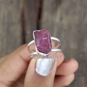 Könnte beinhalten: Ein silberner Ring mit einem rohen, rosafarbenen Rubin-Edelstein, der in der Mitte eingesetzt ist. Der Ring ist ein schlichtes Band mit einem etwas breiteren Band oben, um den Stein zu halten.