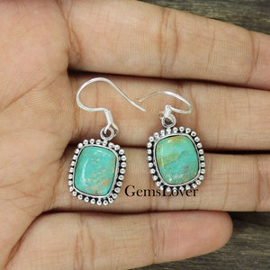 Op de afbeelding: Een paar zilveren oorhangers met turquoise stenen in een vierkante zetting. De stenen hebben een groen en bruin marmerpatroon.
