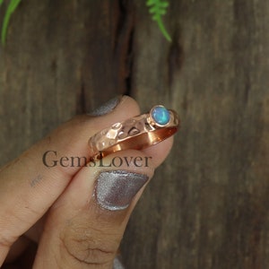 May include: A hammered copper ring with a blue opal gemstone. The ring is a simple design with a smooth band and a single stone.