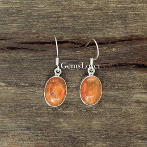 以下が含まれることがあります： 楕円形のオレンジ色の珊瑚石が付いたシルバーのイヤリングのペア。イヤリングはシンプルでエレガントなデザインです。