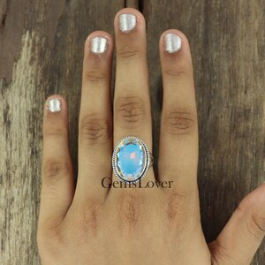 Peut inclure: Une bague en argent avec une grande pierre pr&eacute;cieuse ovale bleue. La pierre pr&eacute;cieuse est taill&eacute;e &agrave; facettes et pr&eacute;sente un effet arc-en-ciel iridescent.