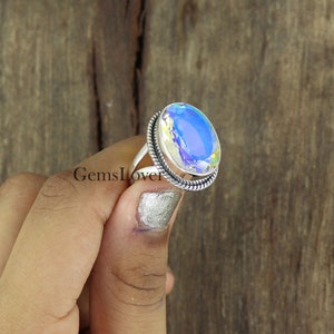 Peut inclure: Une bague en argent avec une grande pierre pr&eacute;cieuse ovale iris&eacute;e. La bague a un design de corde torsad&eacute;e autour de la bande.