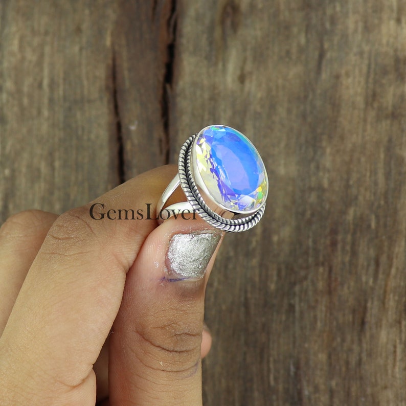 Peut inclure: Une bague en argent avec une grande pierre pr&eacute;cieuse ovale iris&eacute;e. La bague a un design de corde torsad&eacute;e autour de la bande.