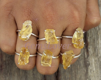 May include: Seven silver rings with yellow gemstone settings. The rings are worn on a person's fingers.