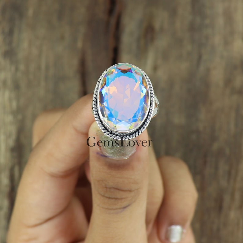 Peut inclure: Une bague en argent avec une grande pierre pr&eacute;cieuse ovale et iris&eacute;e. La pierre pr&eacute;cieuse a une base bleu clair avec des couleurs arc-en-ciel.