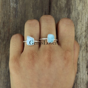 May include: Two silver rings with blue gemstone settings. The rings are on a person's finger.