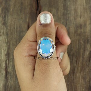 Peut inclure: Une bague en argent avec une grande pierre pr&eacute;cieuse bleue iris&eacute;e de forme ovale. La bague est sertie dans une bande d'argent avec un motif de fil torsad&eacute;.