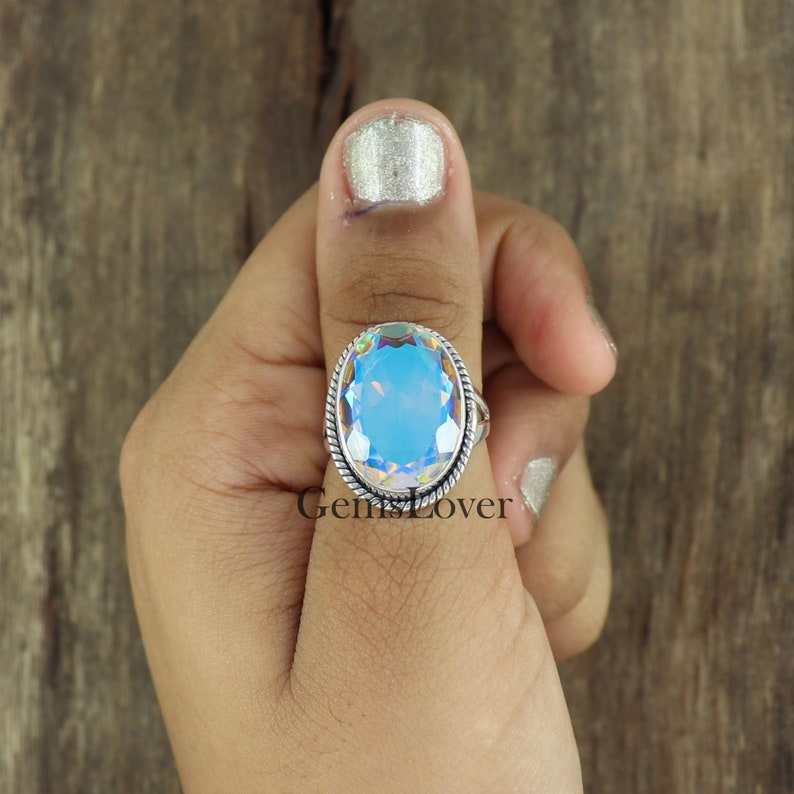 Peut inclure: Une bague en argent avec une grande pierre pr&eacute;cieuse bleue iris&eacute;e de forme ovale. La bague est sertie dans une bande d'argent avec un motif de fil torsad&eacute;.
