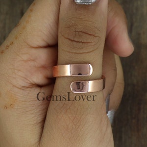 May include: A rose gold colored adjustable ring with a simple, polished design. The ring is shown on a person's thumb.