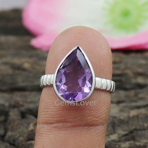 May include: A pear-shaped amethyst gemstone ring set in sterling silver. The ring has a textured band and a purple gemstone.