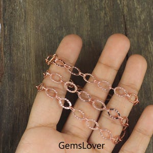 May include: Rose gold chain necklace with oval links, displayed on a hand. The chain has a textured surface and a warm, metallic hue. The text "GemsLover" is visible at the bottom of the image.