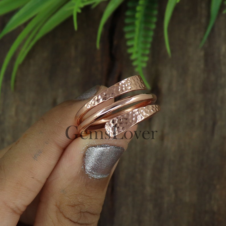 Pode incluir: Um anel de metal martelado em ouro rosa com um design torcido. O anel &eacute; feito de duas bandas que est&atilde;o entrela&ccedil;adas.