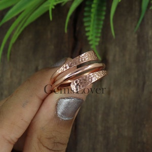 Pode incluir: Um anel de cobre martelado em ouro rosa com um design torcido. O anel &eacute; feito de duas bandas que est&atilde;o entrela&ccedil;adas.