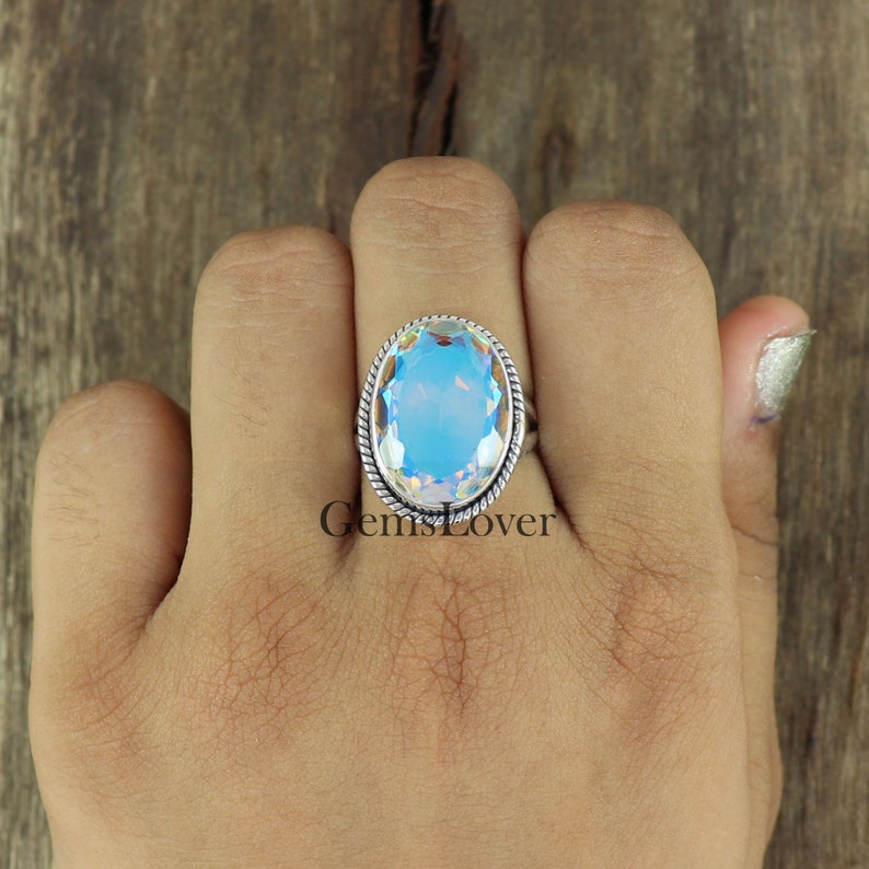 Peut inclure: Une bague en argent avec une grande pierre pr&eacute;cieuse ovale bleue. La pierre pr&eacute;cieuse a un effet arc-en-ciel iridescent. La bague a une bande en argent torsad&eacute;e.