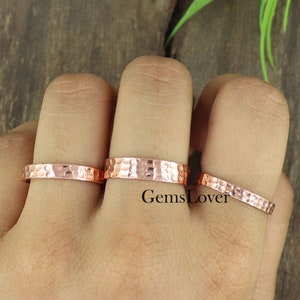May include: Three hammered copper rings of different sizes on a finger. The rings are a warm copper color and have a textured surface.
