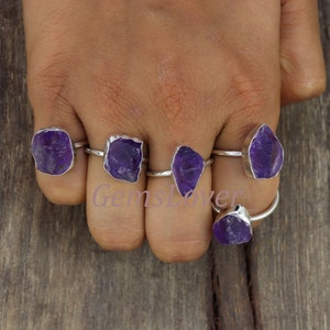 Op de afbeelding: Vijf zilveren ringen met paarse amethist edelstenen. De ringen worden gedragen aan de vingers van een persoon.