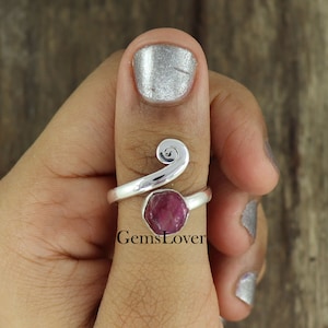 Könnte beinhalten: Ein silberner Daumenring mit einem rosafarbenen Edelstein und einem Spiralendesign. Der Ring wird am Daumen einer Person getragen.