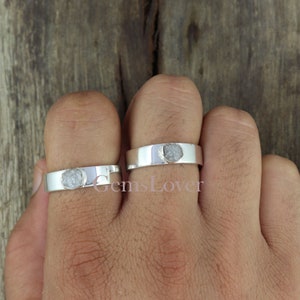 May include: Two silver rings with rough, grey diamond stones set in the centre of each band.