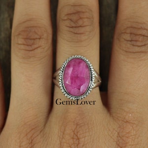 May include: A silver ring with a pink oval gemstone set in a twisted rope design. The ring is on a finger.