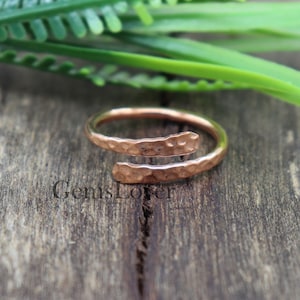 May include: A hammered copper ring with a split band design. The ring is made of a single piece of copper that is bent into a circle and then hammered to create a textured surface.