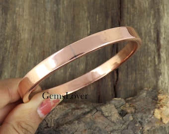 May include: A simple copper bangle bracelet. The bracelet is smooth and shiny, with a slightly rounded edge. It is a classic and timeless design.