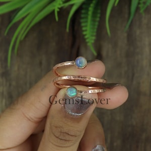 Könnte beinhalten: Zwei zarte Ringe mit gehämmerten Roségoldbändern und schillernden Opal-Edelsteinen. Die Ringe sind übereinander gestapelt und werden an einem Finger getragen.
