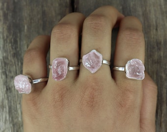May include: Four silver rings with pink rose quartz stones. The rings are on a hand, with the stones facing the camera.