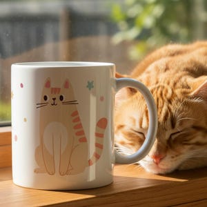 Pode incluir: Uma caneca de cer&acirc;mica branca com uma ilustra&ccedil;&atilde;o de gato de desenho animado em tons de laranja e p&ecirc;ssego, adornada com estrelas e pontos rosa e verdes. Um gato tigrado laranja dormindo ao lado da caneca em uma janela de madeira.