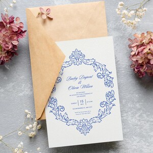Puede incluir: Una invitaci&oacute;n de boda con un dise&ntilde;o floral azul y los nombres "Bailey Dupont & Olivia Wilson" impresos en una tarjeta blanca. La invitaci&oacute;n va acompa&ntilde;ada de un sobre marr&oacute;n y rodeada de flores rosas.