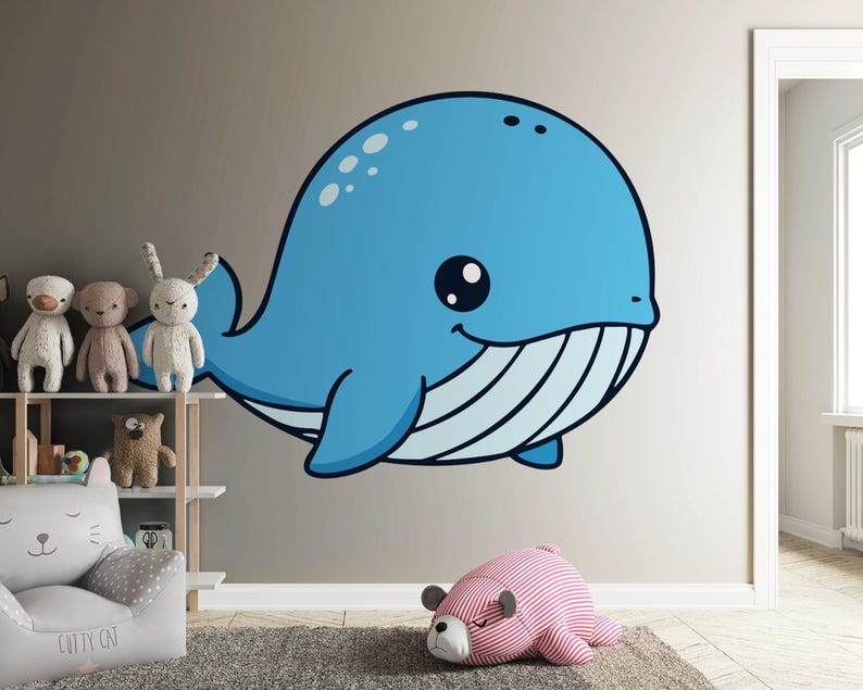 May include: A large, cartoon-style blue whale wall decal with a smiling face and white stripes on its belly. The whale is affixed to a neutral-colored wall in a child's room. Other toys and furniture are visible.