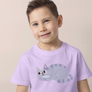 Pode incluir: Uma camiseta lil&aacute;s clara com uma ilustra&ccedil;&atilde;o de gato de desenho animado. O gato &eacute; cinza com listras cinza mais escuras e um nariz rosa. A camiseta &eacute; de manga curta e parece ser feita de um material macio.