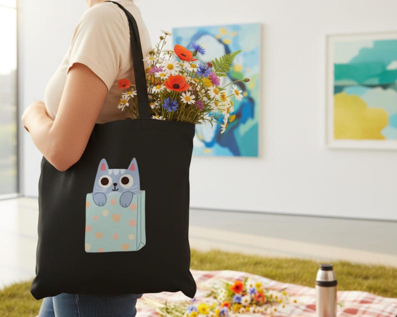 Pode incluir: Bolsa tote preta com um design de gato de desenho animado, cheia de um vibrante buqu&ecirc; de flores. O gato azul claro com olhos grandes espreita de um bolso azul claro decorado com cora&ccedil;&otilde;es rosa. Um acess&oacute;rio elegante e pr&aacute;tico.