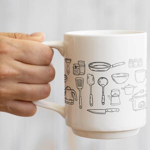 K&ouml;nnte beinhalten: Wei&szlig;e Keramiktasse mit einer schwarzen Strichzeichnung verschiedener K&uuml;chenutensilien und Kochgeschirr. Das Design umfasst eine Bratpfanne, einen Spatel, ein Messer und andere K&uuml;chenwerkzeuge. Die Tasse hat einen gebogenen Griff.