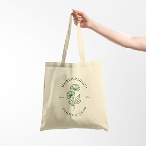 May include: A beige tote bag with a green floral design and the text "Matrios & Lilliana Flower Shop Since 1980" printed on the front.