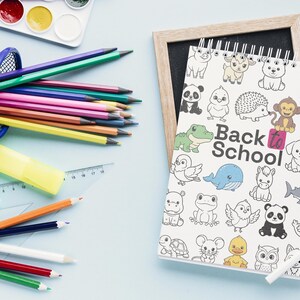 May include: A collection of school supplies on a light blue surface. Includes a wire mesh pencil holder filled with colored pencils, a watercolor paint set, a notebook with animal illustrations and the text "Back to School", and a ruler.