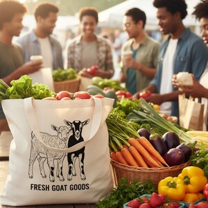 May include: A cream canvas tote bag filled with fresh produce at a market stall. The bag has a goat illustration and reads "FRESH GOAT GOODS". The stall displays tomatoes, lettuce, carrots, peppers, and strawberries. People are browsing the fresh produce.