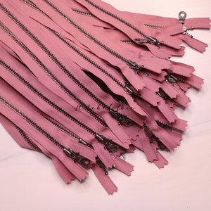 May include: A pile of pink zippers with silver teeth and pulls. The zippers are arranged in a fan shape.